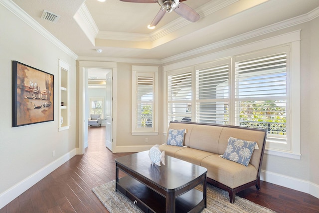 living room featuring dark wood-type flooring, a ceiling fan, baseboards, a tray ceiling, and crown molding