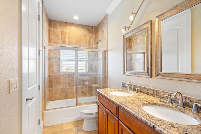 full bath with toilet, double vanity, bath / shower combo with glass door, and a sink