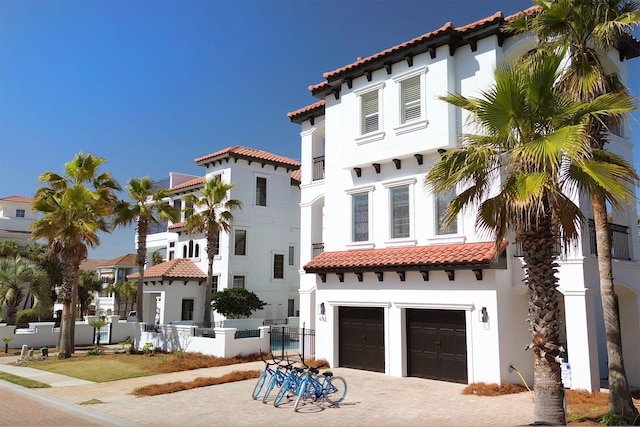 mediterranean / spanish house featuring an attached garage, fence, a tiled roof, decorative driveway, and stucco siding