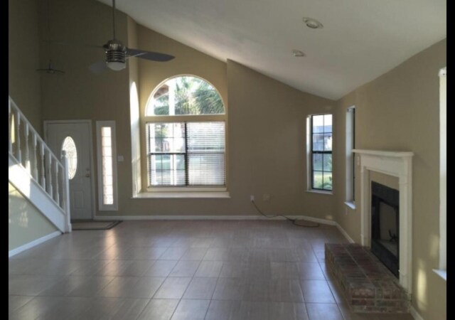 unfurnished living room featuring tile patterned floors, a glass covered fireplace, stairs, and baseboards