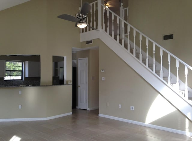 unfurnished living room with stairs, visible vents, a towering ceiling, and a ceiling fan