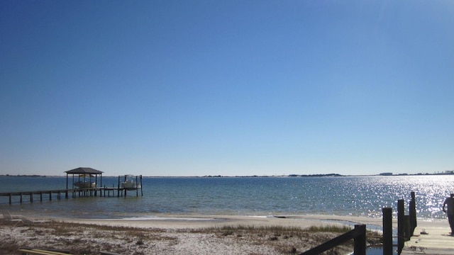 dock area with a water view, boat lift, and a view of the beach