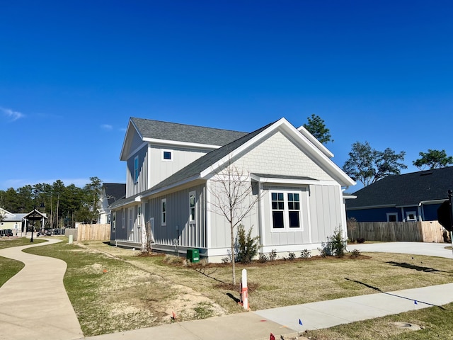 view of front of home with a shingled roof, fence, a front lawn, and board and batten siding