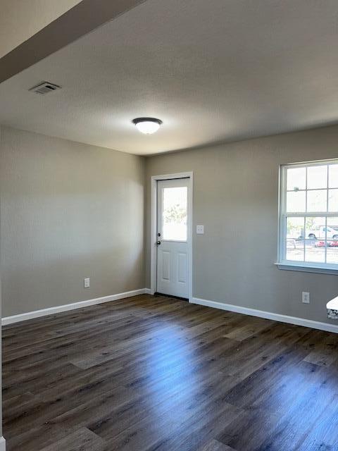 empty room featuring dark wood-style floors, visible vents, and baseboards