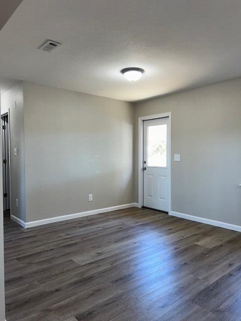 empty room featuring visible vents, dark wood finished floors, and baseboards