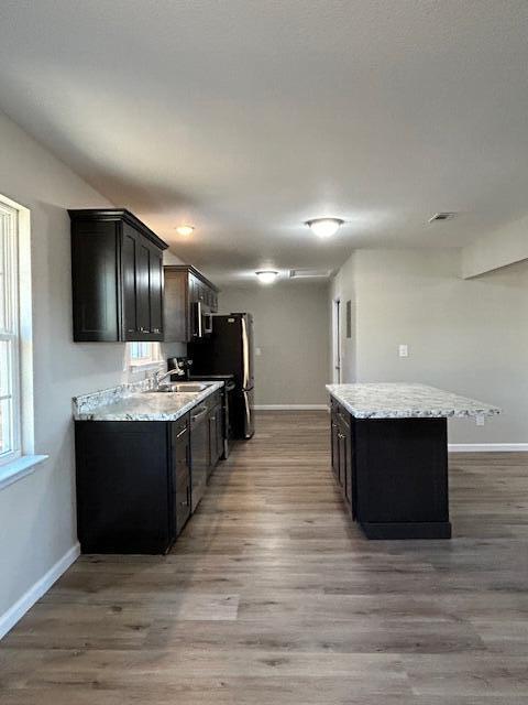 kitchen featuring light wood finished floors, a kitchen island, light stone countertops, and baseboards