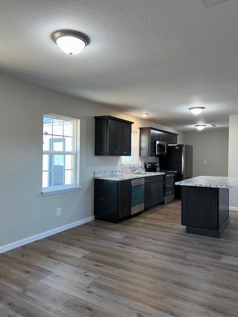 kitchen featuring baseboards, wood finished floors, a center island, stainless steel appliances, and a textured ceiling