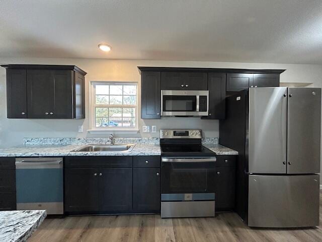 kitchen with stainless steel appliances, a sink, light wood-style flooring, and light stone countertops