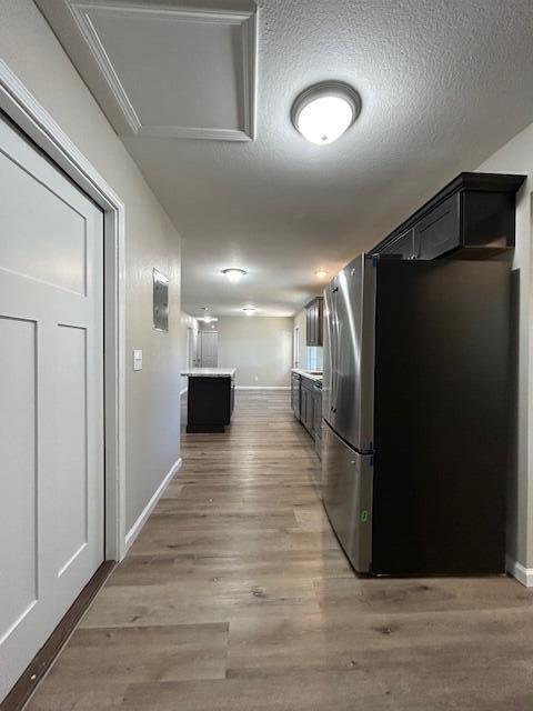 corridor featuring light wood-type flooring, a textured ceiling, and baseboards