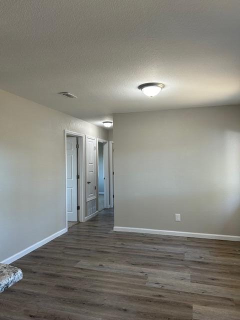 unfurnished room with dark wood-style flooring, visible vents, a textured ceiling, and baseboards