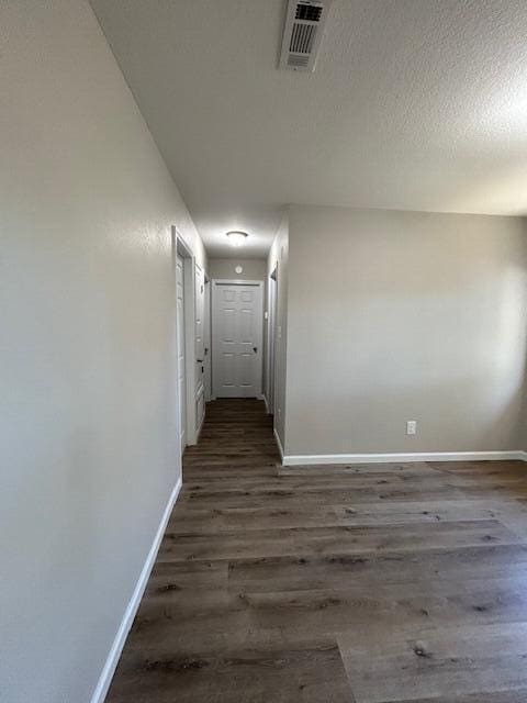 hallway featuring dark wood-type flooring, visible vents, and baseboards