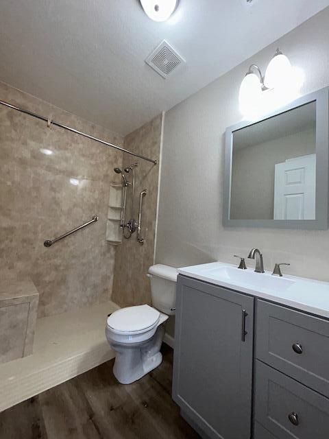 bathroom featuring visible vents, toilet, vanity, wood finished floors, and tiled shower