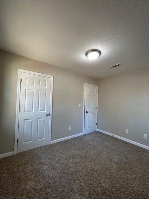 unfurnished bedroom with carpet floors, visible vents, a textured ceiling, and baseboards