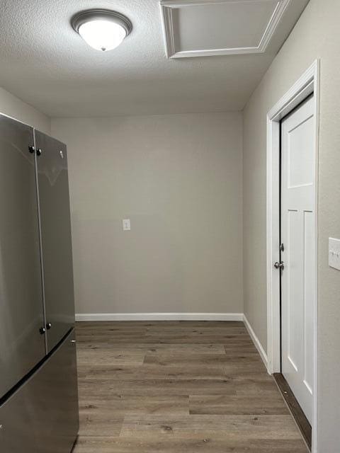 empty room with attic access, a textured ceiling, baseboards, and wood finished floors