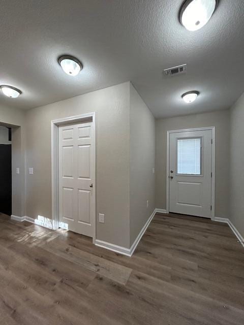 entryway featuring a textured ceiling, wood finished floors, visible vents, and baseboards