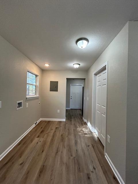 corridor with a textured ceiling, electric panel, baseboards, and wood finished floors