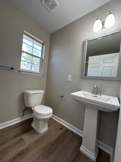 half bath featuring visible vents, toilet, a sink, wood finished floors, and baseboards