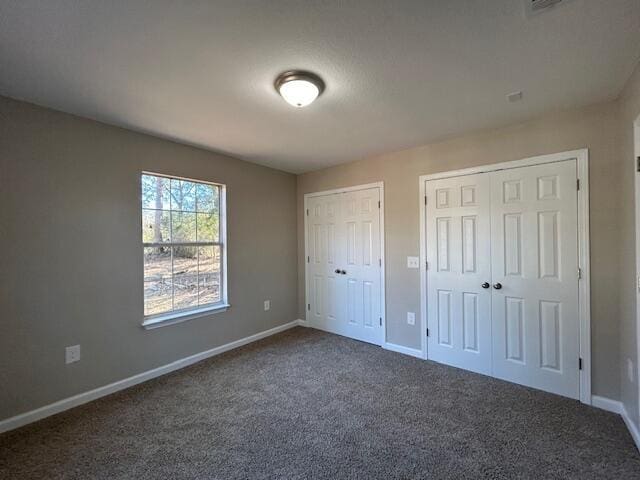 unfurnished bedroom featuring multiple closets, dark carpet, and baseboards