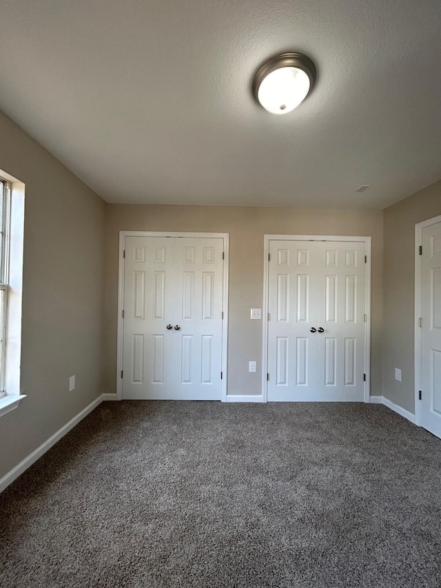 unfurnished bedroom featuring carpet, baseboards, and two closets