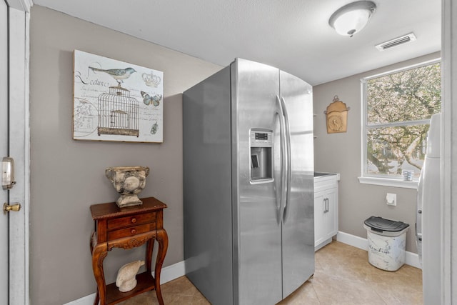 kitchen featuring light tile patterned floors, visible vents, baseboards, stainless steel fridge with ice dispenser, and white cabinets