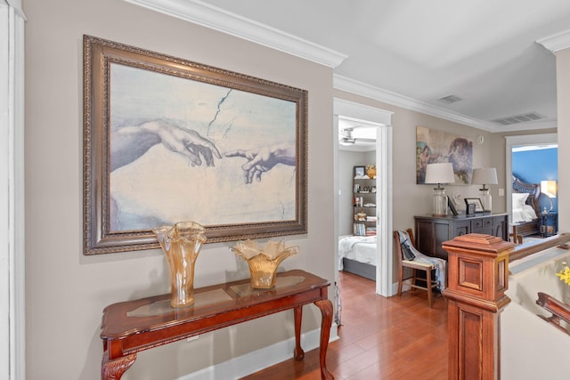 hall with visible vents, wood finished floors, baseboards, and ornamental molding