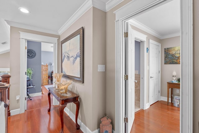 corridor featuring visible vents, baseboards, wood finished floors, and ornamental molding