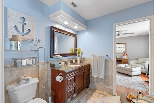 bathroom with visible vents, a wainscoted wall, toilet, tile walls, and vanity