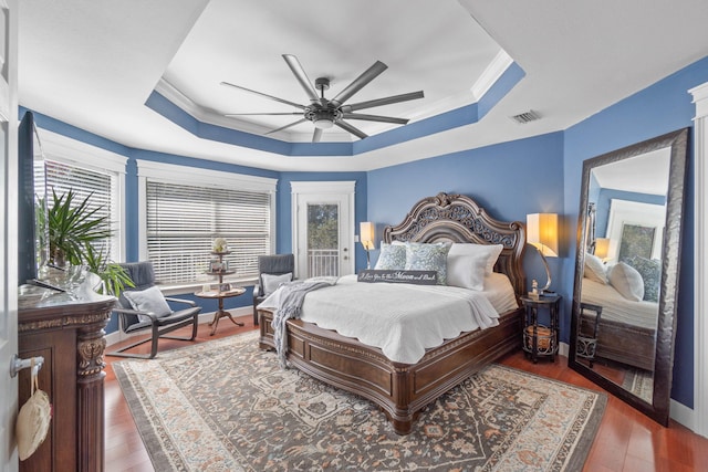 bedroom featuring a raised ceiling, wood finished floors, visible vents, and ornamental molding