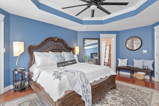 bedroom with a ceiling fan, a tray ceiling, wood finished floors, crown molding, and baseboards