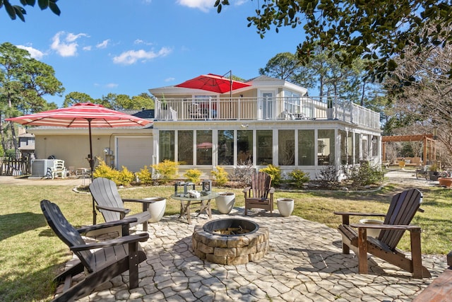 back of house featuring a balcony, a yard, a fire pit, a garage, and a patio area