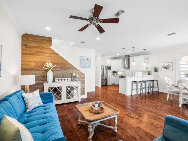 living room with visible vents, dark wood-type flooring, wooden walls, and ornamental molding