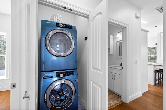 clothes washing area featuring stacked washer / drying machine, visible vents, wood finished floors, and laundry area