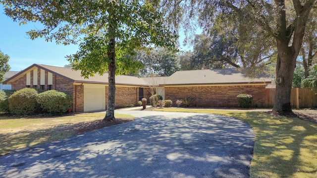 view of front of property with driveway, brick siding, an attached garage, and fence