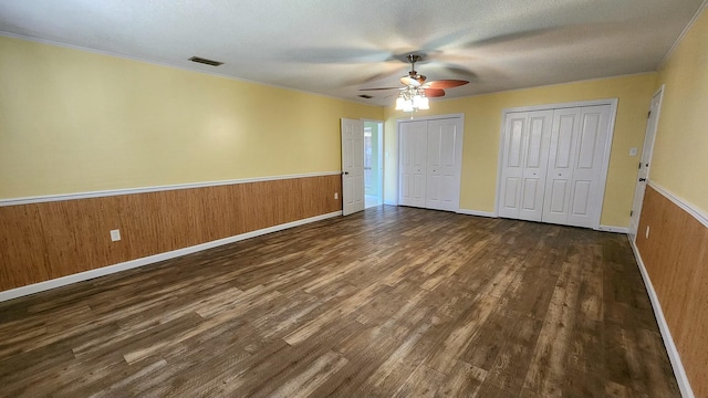 unfurnished bedroom with visible vents, a wainscoted wall, dark wood-style floors, wood walls, and two closets