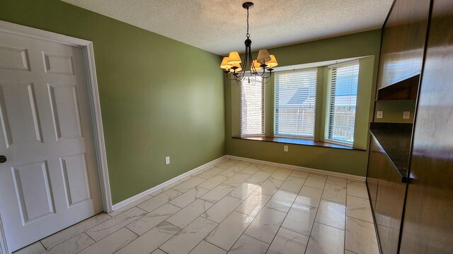 unfurnished dining area with a chandelier, marble finish floor, a textured ceiling, and baseboards