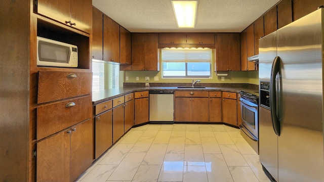 kitchen with dark countertops, under cabinet range hood, appliances with stainless steel finishes, and a sink