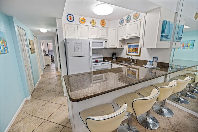 kitchen with white cabinetry, a sink, dark stone countertops, white appliances, and a peninsula