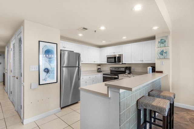 kitchen featuring visible vents, white cabinets, appliances with stainless steel finishes, a kitchen breakfast bar, and a peninsula