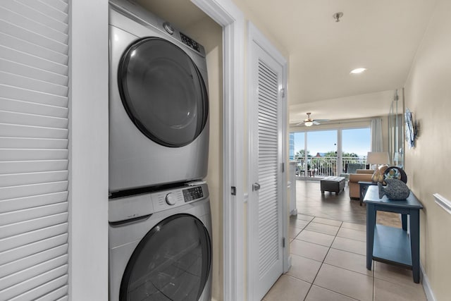 laundry room with a ceiling fan, stacked washer / dryer, light tile patterned flooring, laundry area, and baseboards