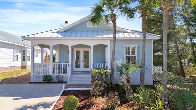 bungalow-style house featuring french doors, a chimney, a porch, a standing seam roof, and metal roof