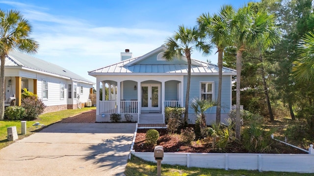 view of front facade with metal roof, a porch, french doors, a standing seam roof, and a chimney