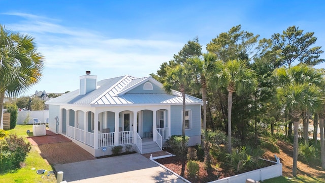 view of front of home with metal roof, covered porch, fence, driveway, and a standing seam roof