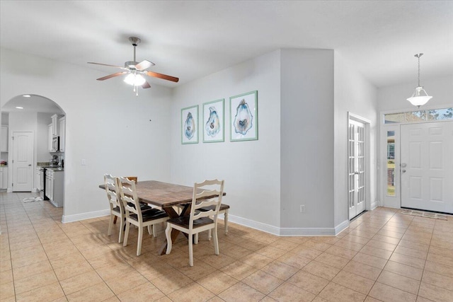 dining room with a ceiling fan, arched walkways, baseboards, and light tile patterned floors