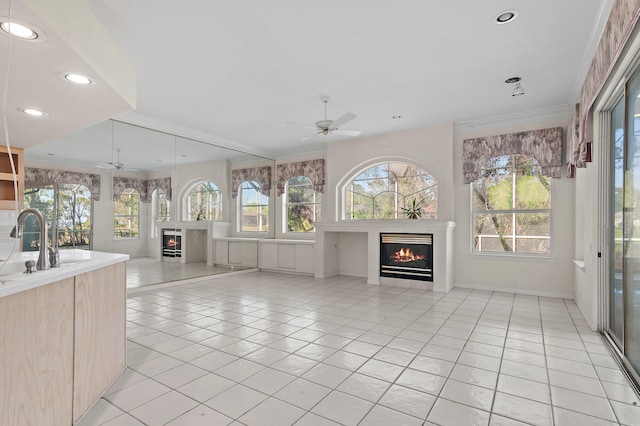 unfurnished living room with light tile patterned floors, plenty of natural light, ceiling fan, and a lit fireplace