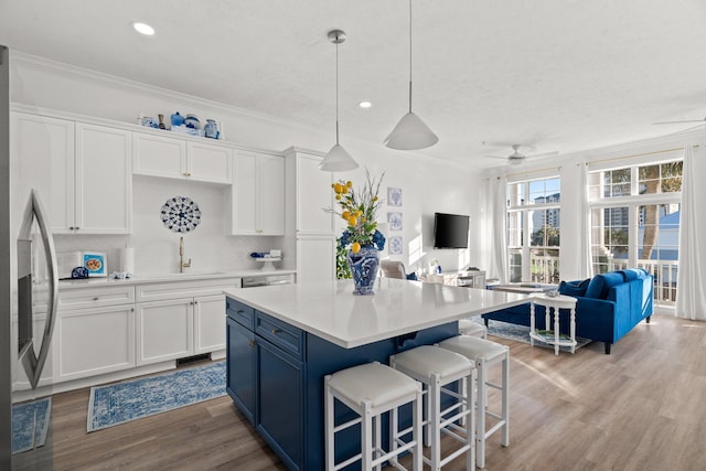 kitchen with open floor plan, ornamental molding, stainless steel refrigerator with ice dispenser, wood finished floors, and white cabinets