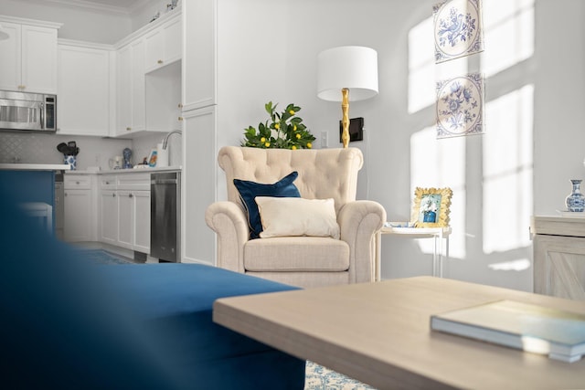 kitchen featuring stainless steel microwave, white cabinetry, light countertops, and ornamental molding