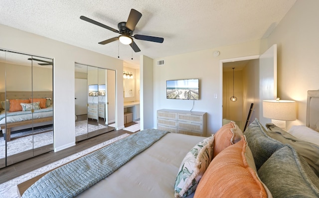 bedroom featuring a textured ceiling, wood finished floors, two closets, and visible vents