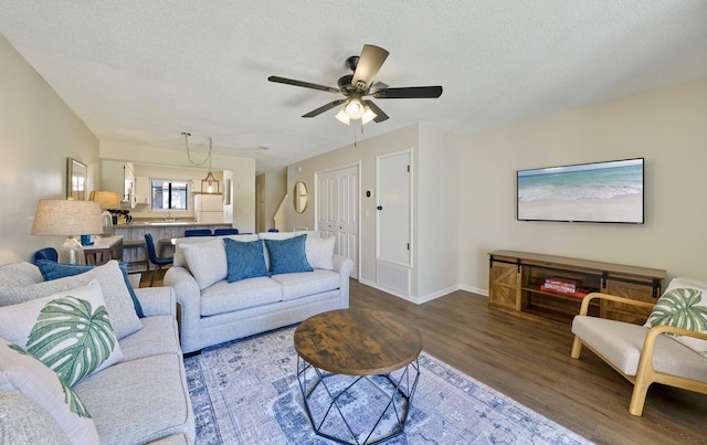 living room with ceiling fan, a textured ceiling, baseboards, and wood finished floors