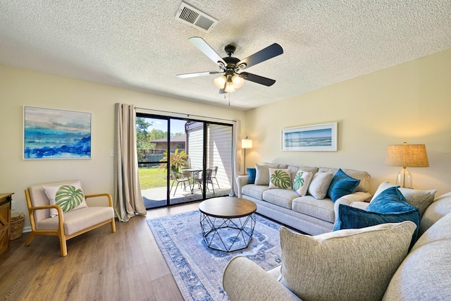 living room with ceiling fan, a textured ceiling, wood finished floors, and visible vents