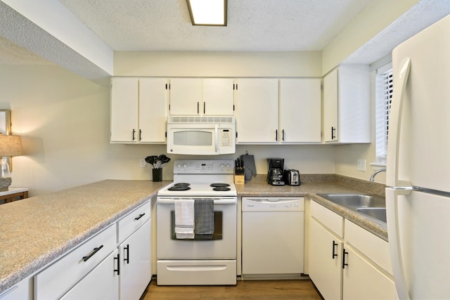 kitchen featuring white cabinetry, a sink, a textured ceiling, wood finished floors, and white appliances